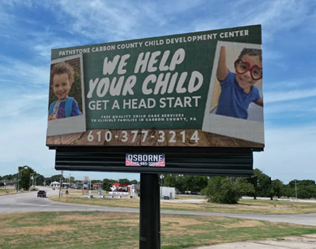 An LED roadside sign displays "Free quality child care for eligible Carbon County, PA families" with two smiling children pictured.
