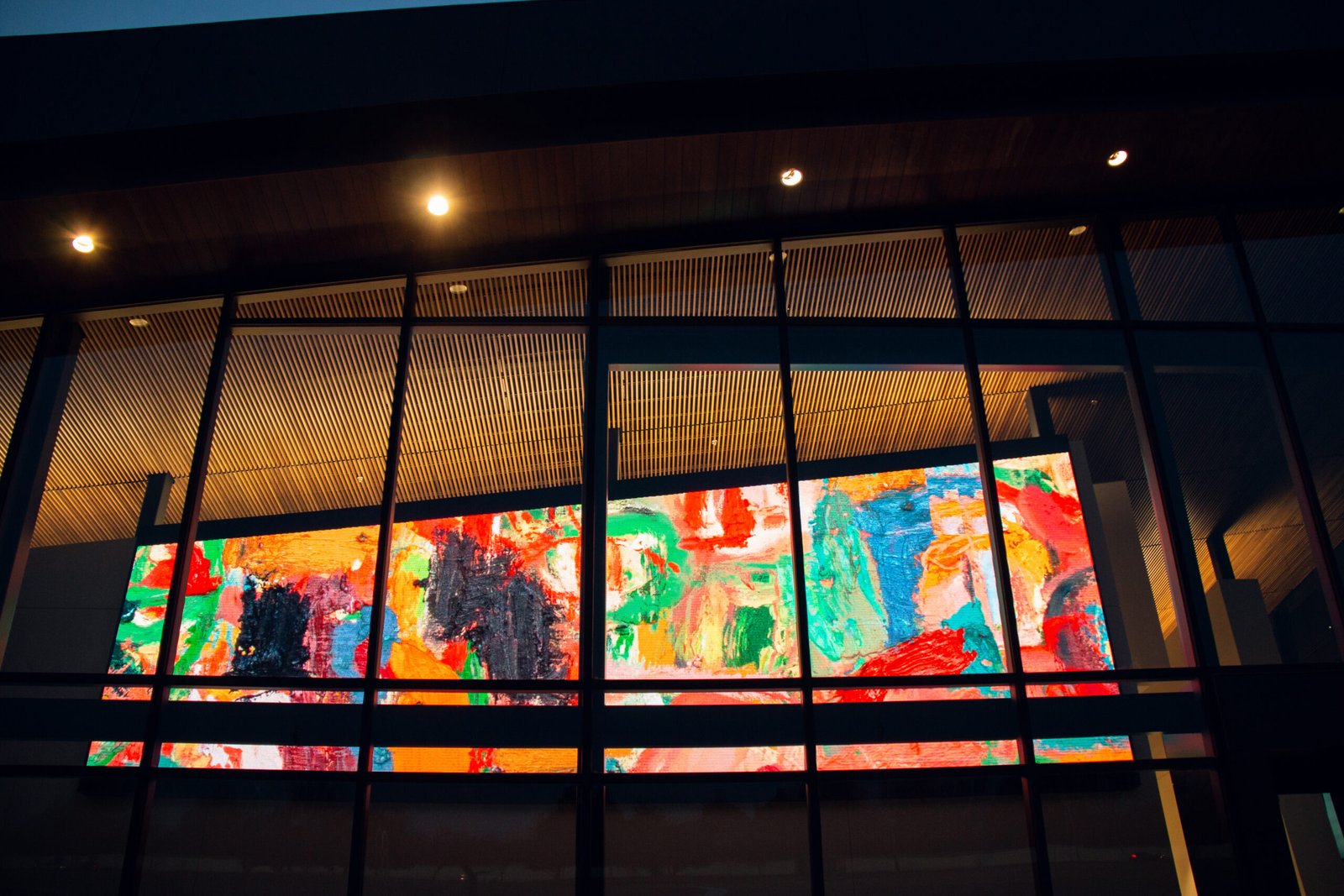 A large LED display behind the glass façade at Mark Arts shows bright multicolored abstract artwork at night, with the building's dark window framing visible.