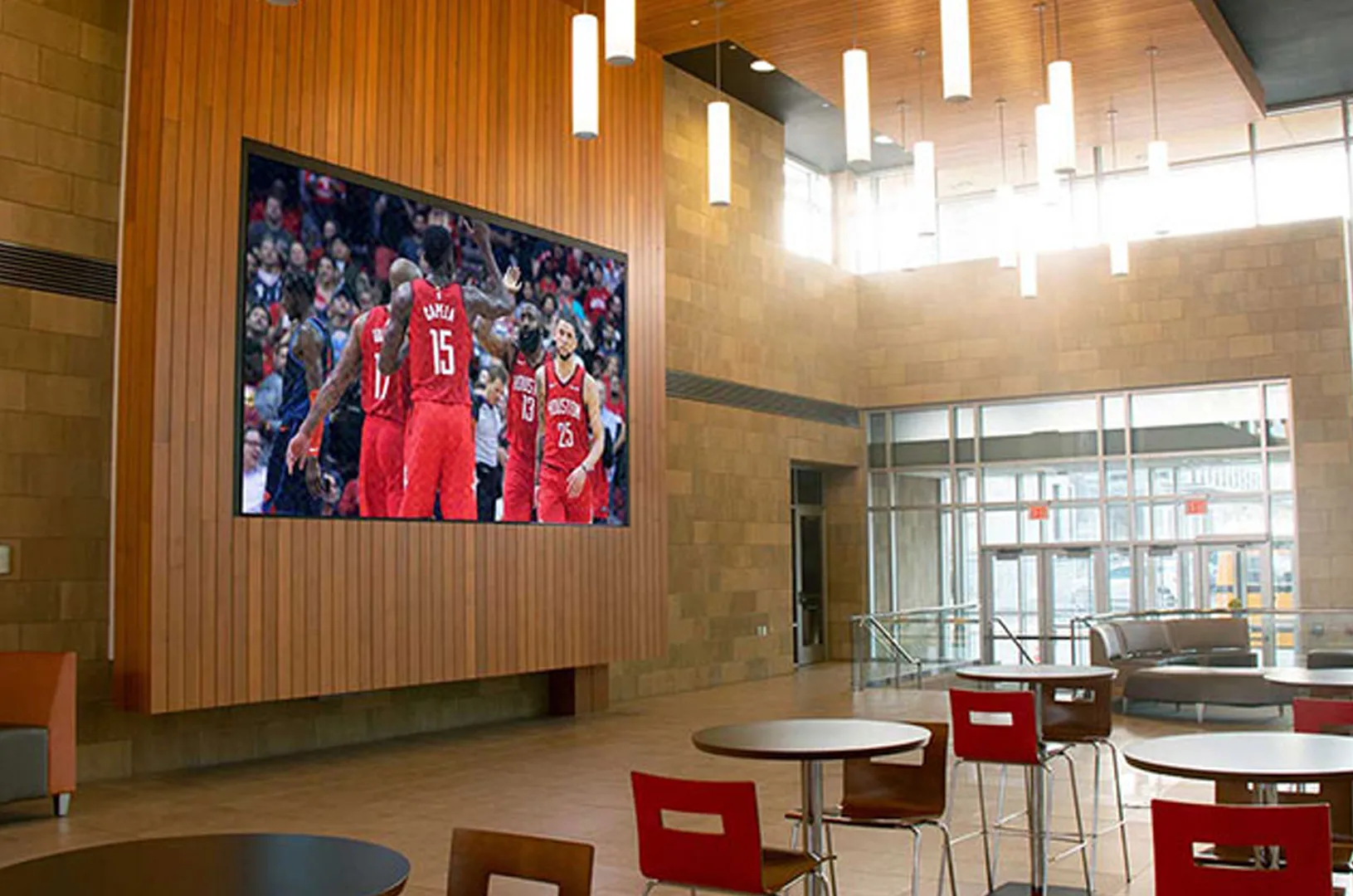 Large indoor LED display shows a group in red shirts above cafe-style tables and seating in the Downtown YMCA lobby.