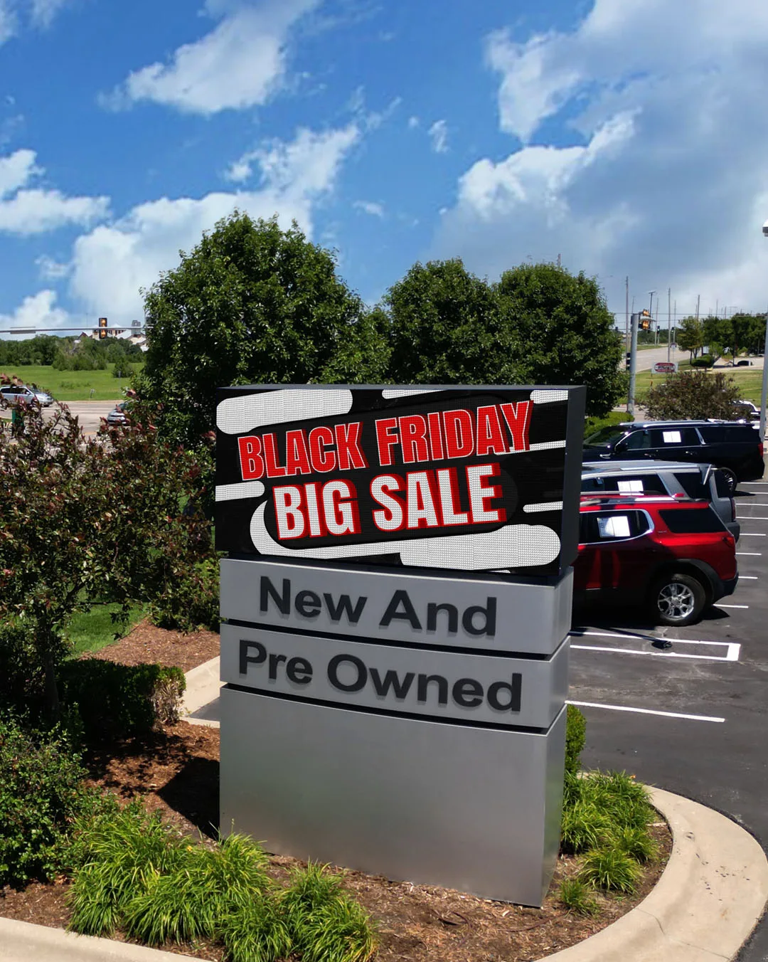 A low monument sign for Hatchett GMC includes an LED display with a big-sale message above new-and-pre-owned lettering, with parked vehicles behind it.