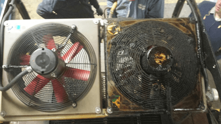 Two electronic cooling fans side by side; left is clean and red, right is oily. Workers in uniforms visible near LED sign background.