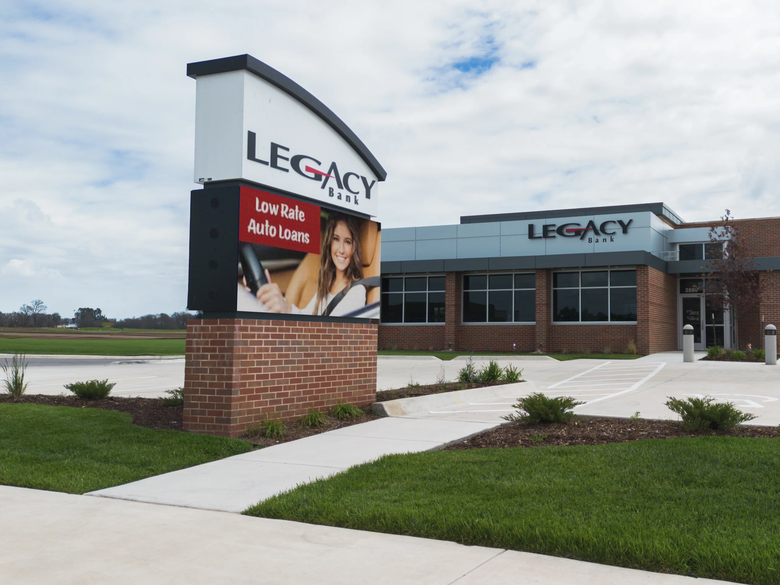Modern bank with LEGACY BANK channel letter signage and high-brightness LED message center showing auto loan ad; landscaped grounds.