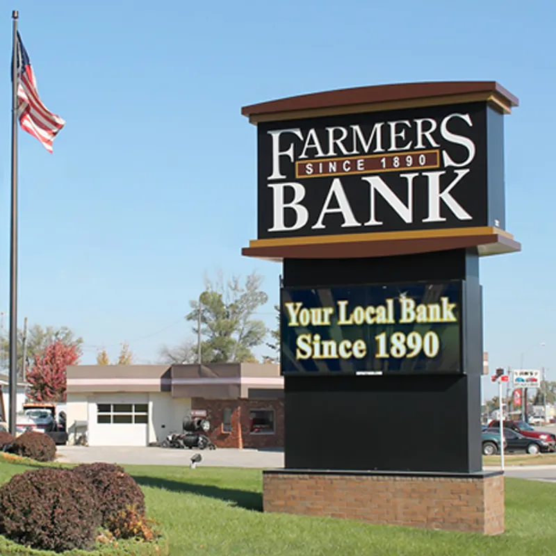 FLEX a high-brightness LED electronic message center sign for Farmers Bank displays "Farmers Bank Since 1890" and "Your Local Bank Since 1890." An American flag and a small building appear in the background.