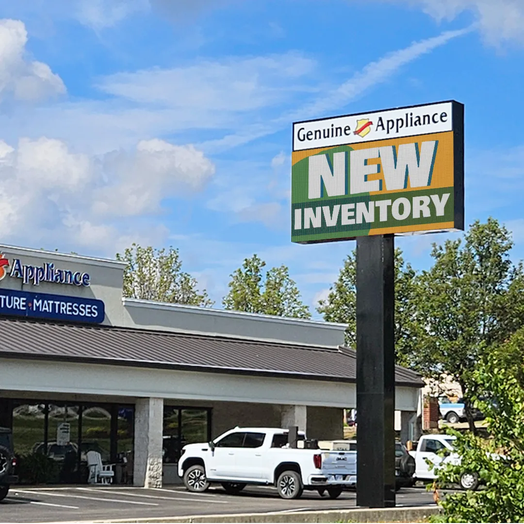Genuine Appliance storefront with an LED electronic message center displaying NEW INVENTORY, visible above parked vehicles under a blue sky with scattered clouds.