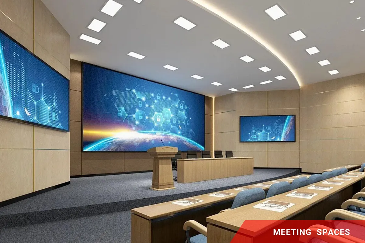 A well-lit conference room featuring high-brightness LED signage, including large electronic message centers at the front, a podium, and chairs arranged in rows. The wood-paneled walls provide a modern backdrop, and an aluminum-framed red solid-state sign in the corner displays MEETING SPACES.