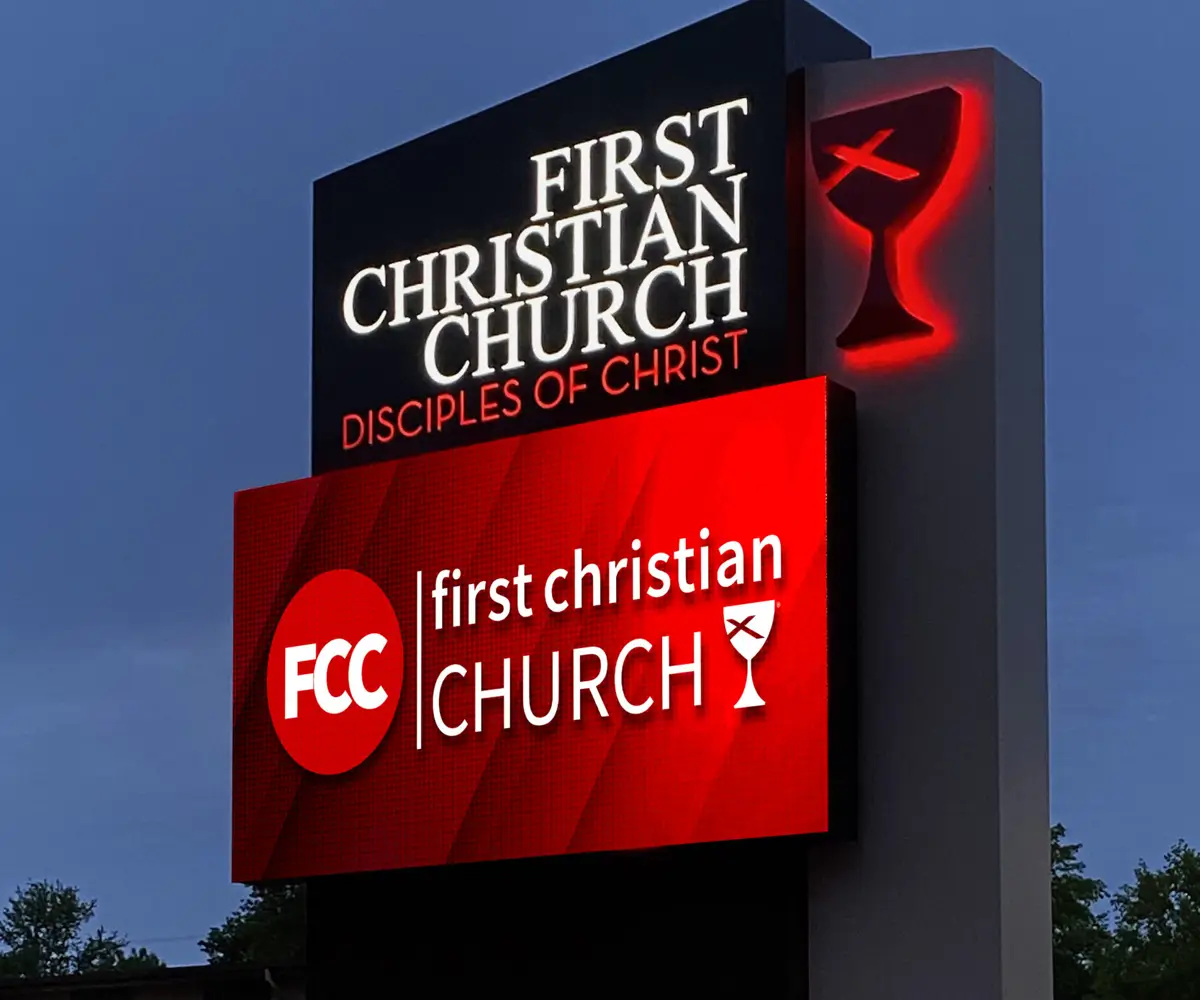 An illuminated LED electronic message center for First Christian Church, Disciples of Christ, features the church name and a red chalice logo on both display panels; solid-state high-brightness construction, positioned outdoors with sky and trees visible in the background.