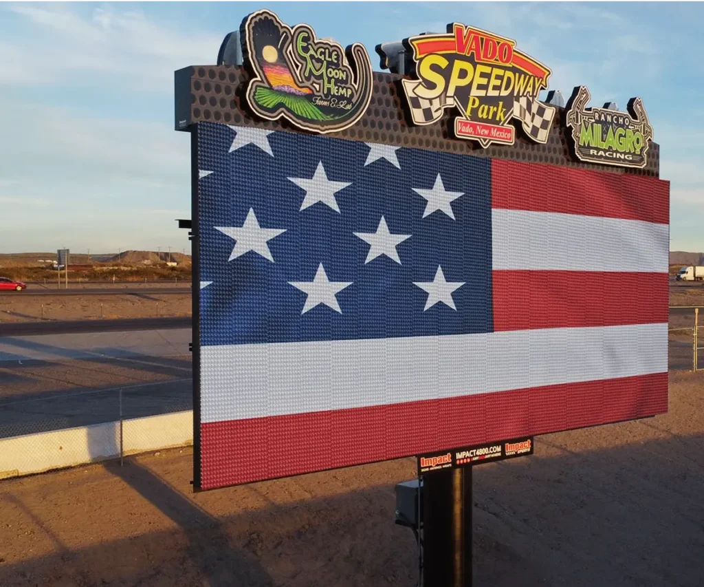 A high-brightness LED electronic message center at Vado Speedway Park shows a digital American flag image against clear desert skies, mounted on a durable aluminum frame.