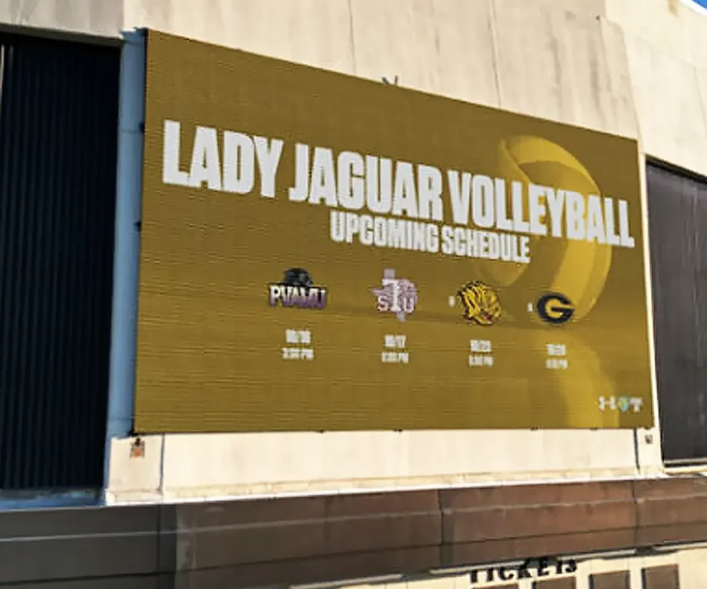 High-brightness yellow LED electronic message center mounted on a building shows Lady Jaguar Volleyball Upcoming Schedule, with team logos, match dates, and times for four opponents. Solid-state display features background volleyball graphic.