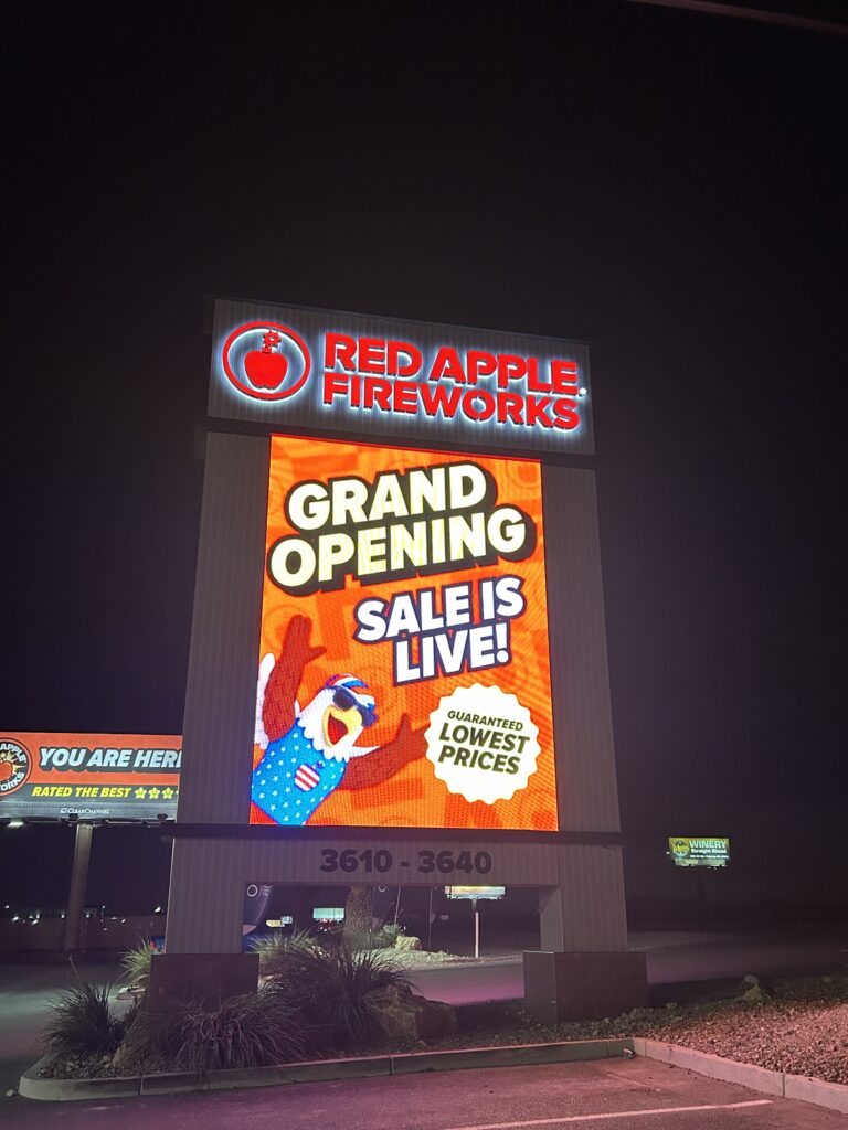 LED electronic message center for Red Apple Fireworks illuminated at night, showing “Grand Opening Sale is Live! Guaranteed lowest prices” text. The display features a cartoon eagle in a patriotic outfit and the address range 3610–3640 clearly visible at the bottom.