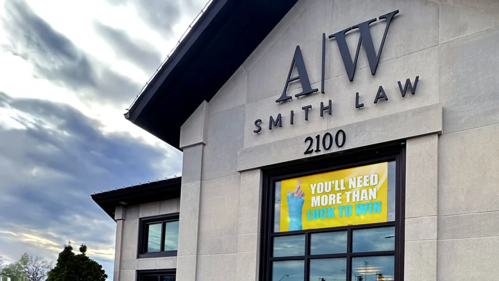 Gray commercial building with large A.W. Smith Law 2100 channel lettering on the facade and a high-brightness yellow electronic message center in the window displaying, “You’ll need more than luck to win,” set against a cloudy sky.