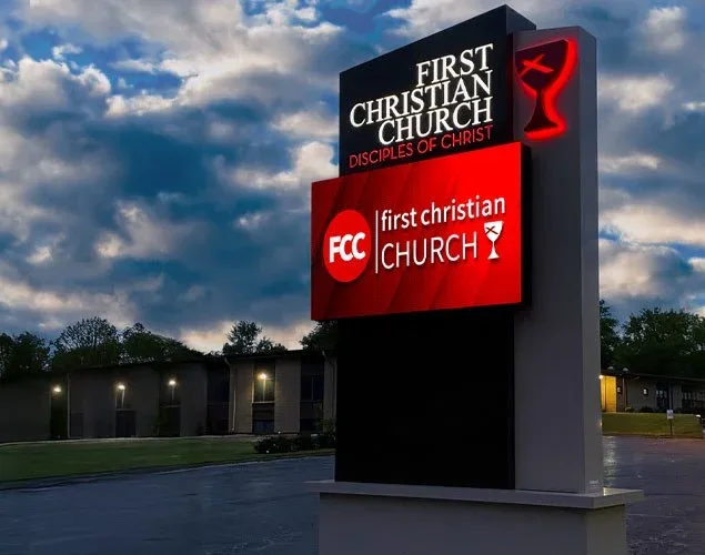First Christian Church monument sign with white church lettering on a red LED display beneath a permanent church name and chalice topper at dusk.