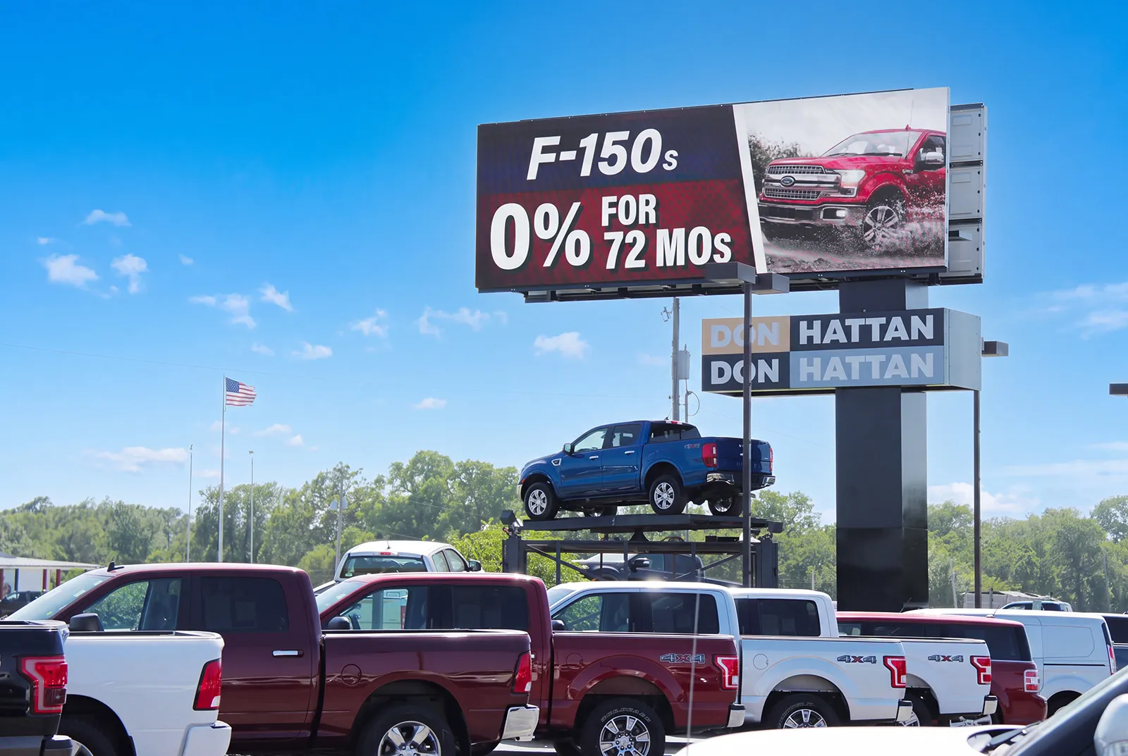 Don Hattan Ford LED display showing an F-150 promotion above a blue pickup on a platform and parked trucks in Augusta, Kansas.