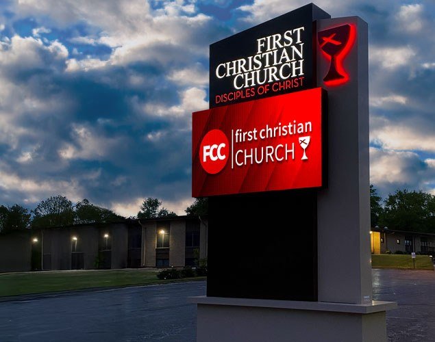 First Christian Church monument sign with an illuminated church name, red chalice emblem, and LED display showing the church logo at dusk.