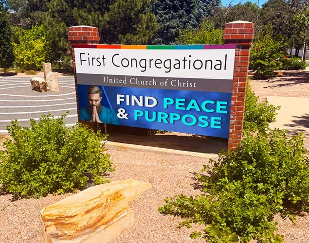 First Congregational United Church of Christ sign between brick pillars, with an LED display reading “Find Peace & Purpose” beside landscaped grounds.