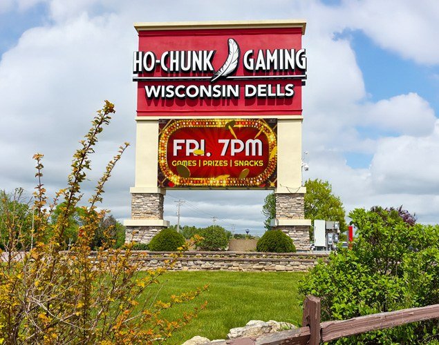 Ho-Chunk Gaming Wisconsin Dells roadside sign with an LED display advertising Friday games, prizes, and snacks amid landscaped greenery.