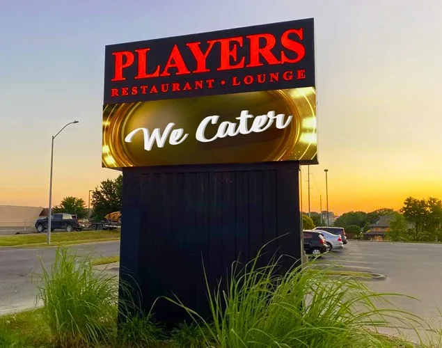 Players Restaurant and Lounge monument shows We Cater on its illuminated LED display at sunset, with plants around the sign's base.