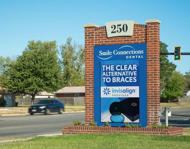 Smile Connections Family Dentistry monument shows a clear-aligner promotion on a vertical LED display beneath the practice name and street number.